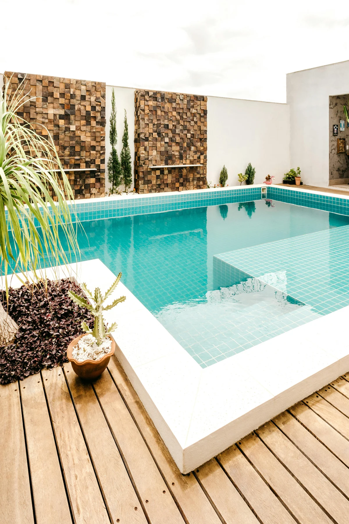 Pool mit türkisfarbenem Wasser, Natursteinwand und Holzterrasse